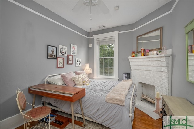 bedroom with ceiling fan, a fireplace, visible vents, and wood finished floors