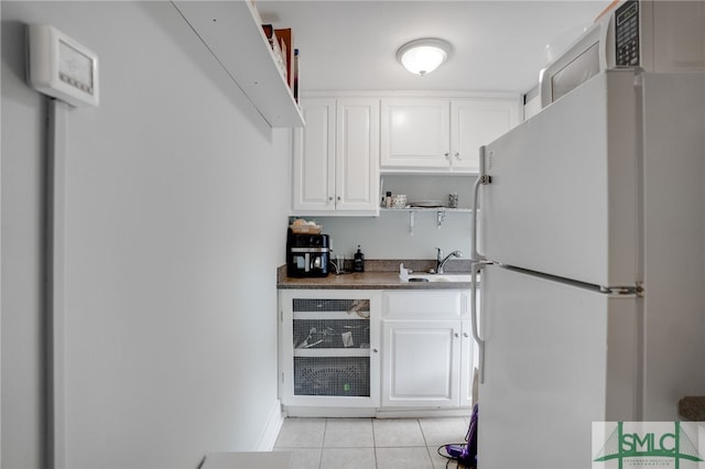 kitchen with light tile patterned floors, dark countertops, freestanding refrigerator, white cabinets, and a sink