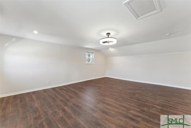 spare room featuring dark wood-style floors, lofted ceiling, attic access, and baseboards