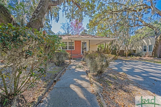 view of front facade featuring a carport, driveway, brick siding, and fence