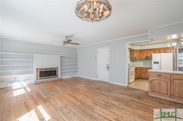 unfurnished living room with ceiling fan with notable chandelier, a glass covered fireplace, light wood-style flooring, and crown molding