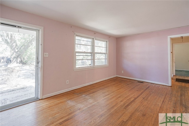 spare room featuring wood-type flooring, visible vents, and baseboards