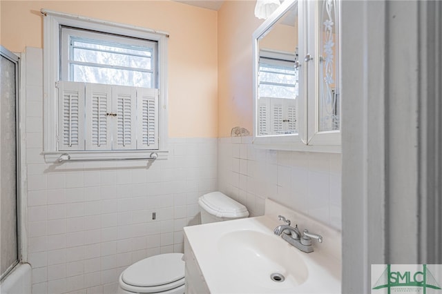 bathroom featuring toilet, a shower with door, a wainscoted wall, vanity, and tile walls