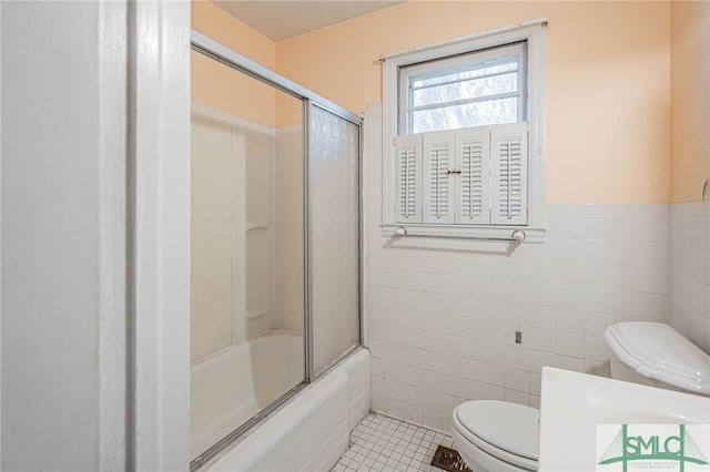 full bath with tile walls, toilet, wainscoting, combined bath / shower with glass door, and tile patterned flooring