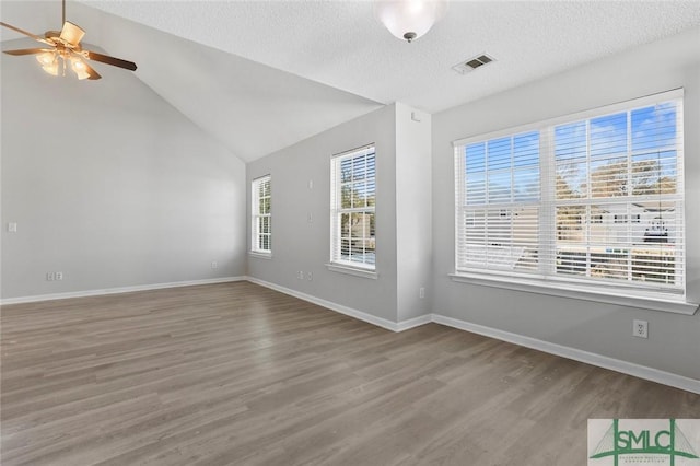 empty room featuring wood finished floors, a ceiling fan, visible vents, vaulted ceiling, and baseboards