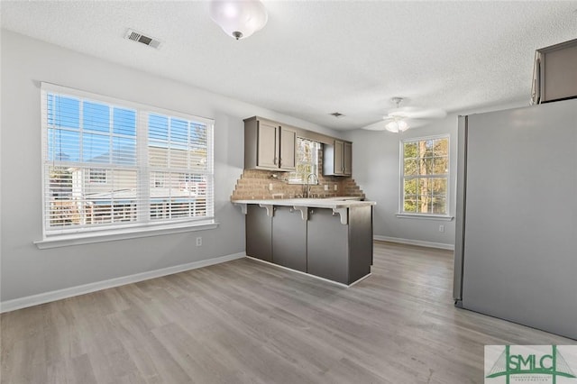 kitchen featuring visible vents, decorative backsplash, a peninsula, light wood-style floors, and a sink