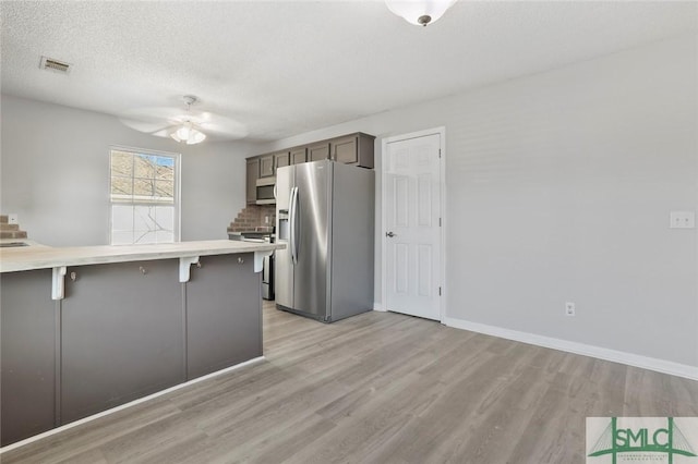 kitchen featuring light countertops, appliances with stainless steel finishes, a breakfast bar area, and light wood-style floors