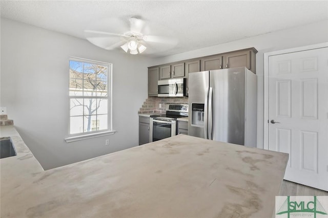 kitchen featuring appliances with stainless steel finishes, a ceiling fan, a peninsula, and tasteful backsplash