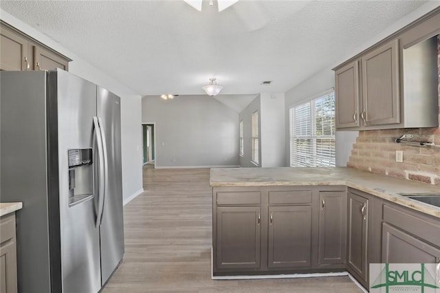 kitchen with light countertops, decorative backsplash, light wood-type flooring, a peninsula, and stainless steel fridge with ice dispenser