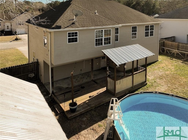 rear view of property with fence, a wooden deck, and an outdoor pool