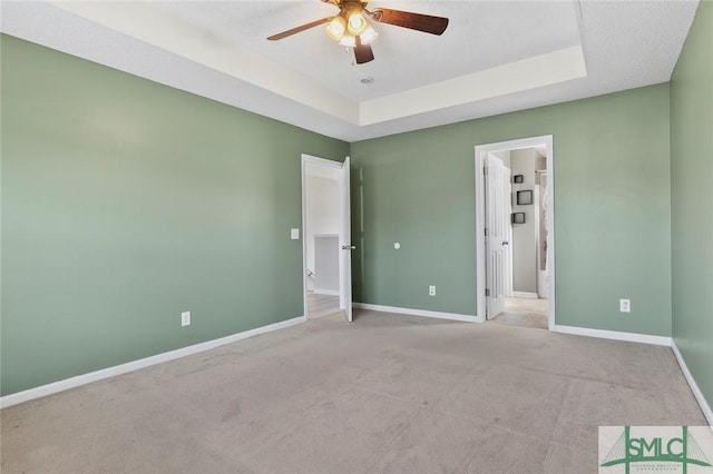 unfurnished bedroom featuring carpet floors, a raised ceiling, a ceiling fan, and baseboards