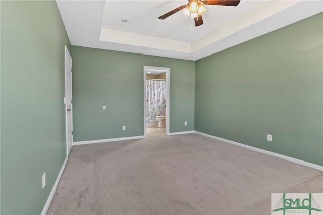 empty room with carpet flooring, a raised ceiling, a ceiling fan, and baseboards