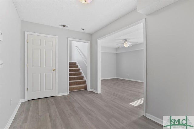 spare room featuring visible vents, stairway, ceiling fan, wood finished floors, and baseboards