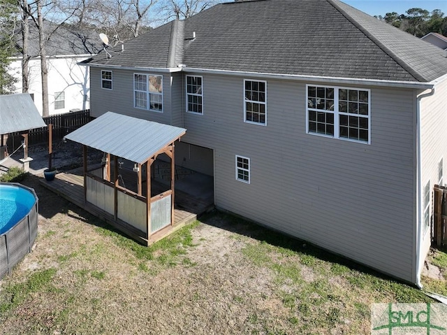 back of house with roof with shingles, fence, and a wooden deck