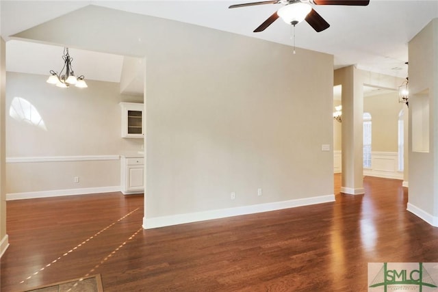 empty room with vaulted ceiling, dark wood finished floors, baseboards, and ceiling fan with notable chandelier