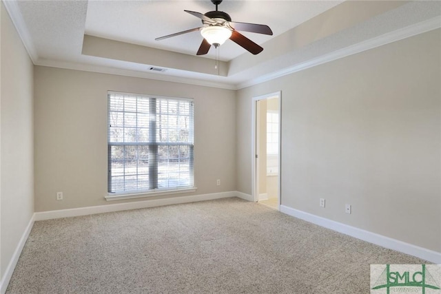 carpeted empty room with visible vents, baseboards, a raised ceiling, ceiling fan, and ornamental molding