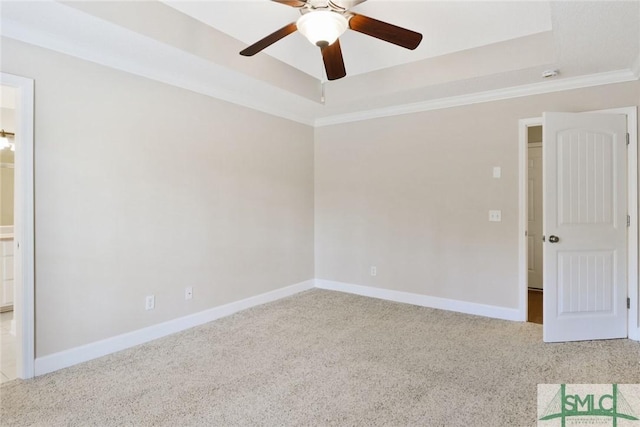 empty room with a tray ceiling, light colored carpet, crown molding, and baseboards