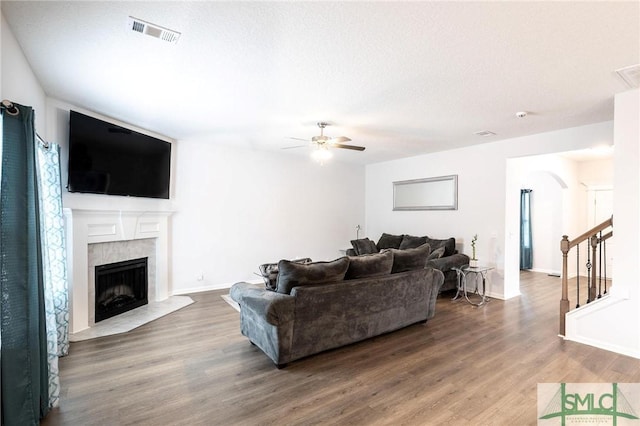 living room with visible vents, a ceiling fan, a tiled fireplace, wood finished floors, and stairs