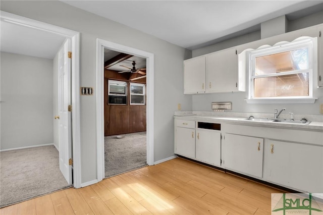 kitchen with baseboards, white cabinets, light countertops, light wood-type flooring, and a sink