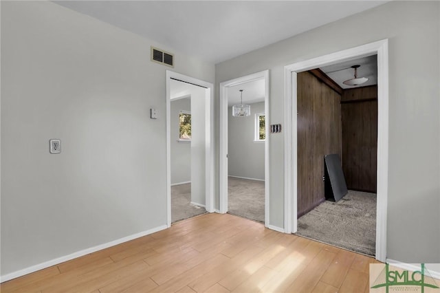 corridor featuring light wood-type flooring, visible vents, and baseboards