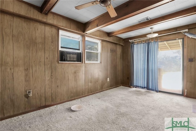 empty room featuring wooden walls, carpet floors, a ceiling fan, visible vents, and beamed ceiling