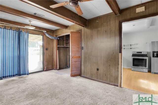 unfurnished living room featuring carpet floors, wood walls, beamed ceiling, and visible vents