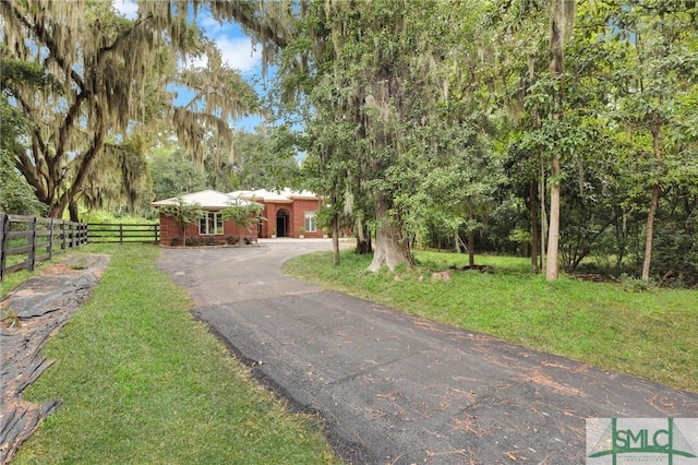 view of front of house featuring aphalt driveway, brick siding, fence, and a front lawn