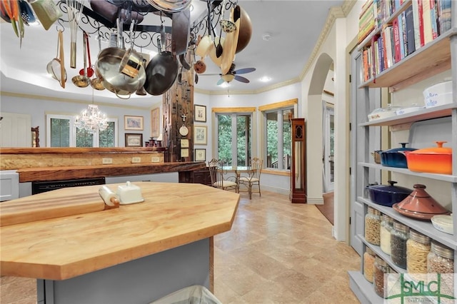 kitchen featuring baseboards, arched walkways, wood counters, crown molding, and ceiling fan with notable chandelier