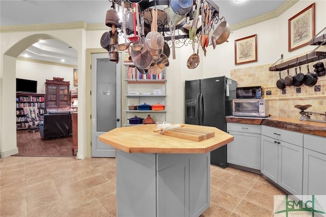 kitchen featuring arched walkways, butcher block countertops, black fridge, decorative backsplash, and crown molding