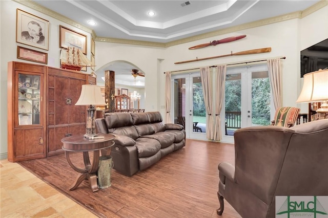 living area with arched walkways, a towering ceiling, a tray ceiling, and wood finished floors