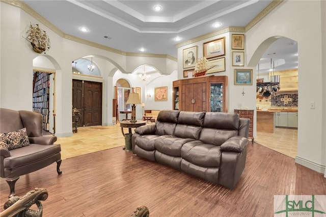 living area with a tray ceiling, light wood finished floors, visible vents, ornamental molding, and a chandelier