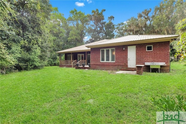 back of property with metal roof, brick siding, a yard, and covered porch