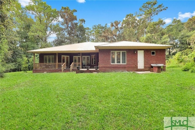 rear view of property with metal roof, a yard, a porch, and brick siding