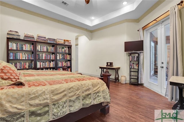 bedroom featuring arched walkways, wood finished floors, visible vents, access to exterior, and a raised ceiling