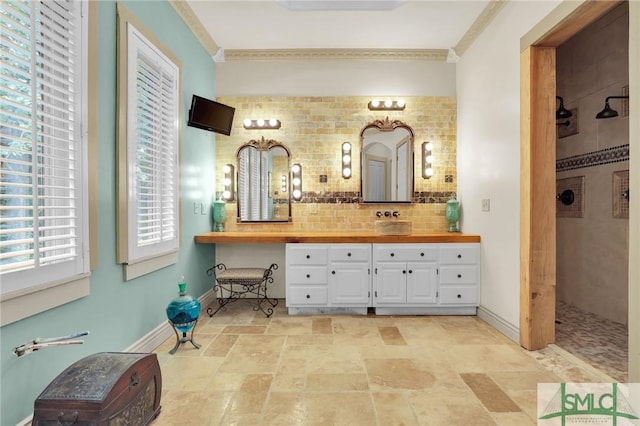 bathroom with a walk in shower, vanity, baseboards, backsplash, and stone finish flooring