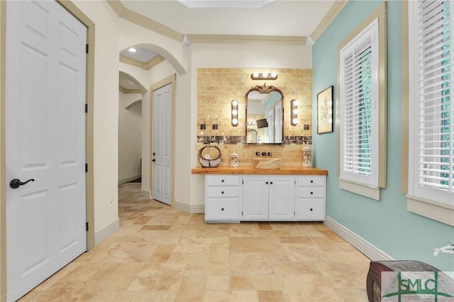 bathroom featuring baseboards, crown molding, vanity, and decorative backsplash