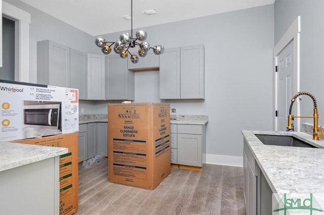 kitchen with light wood-style flooring, light stone counters, stainless steel microwave, gray cabinetry, and a sink