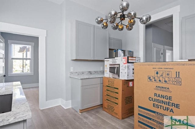 interior space with white microwave, baseboards, light wood-type flooring, gray cabinets, and an inviting chandelier