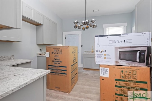 kitchen with decorative light fixtures, light wood finished floors, stainless steel microwave, an inviting chandelier, and light stone countertops