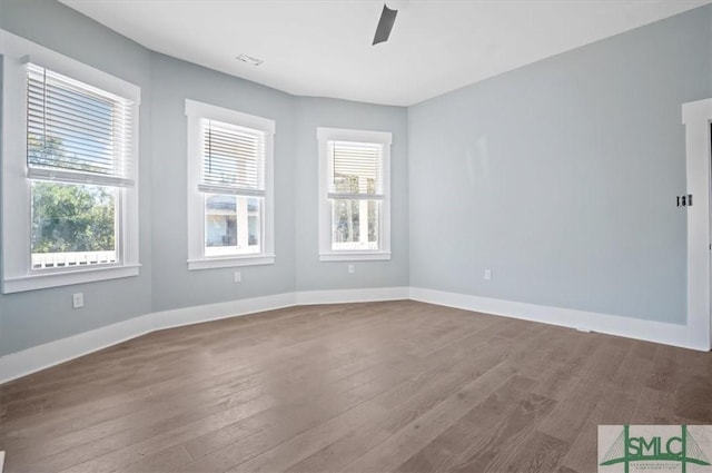 empty room featuring a healthy amount of sunlight, baseboards, and wood finished floors