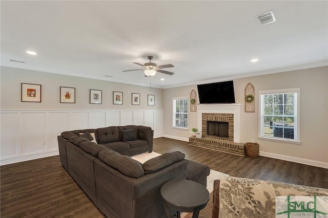 living area with a fireplace, visible vents, dark wood-style flooring, and ornamental molding