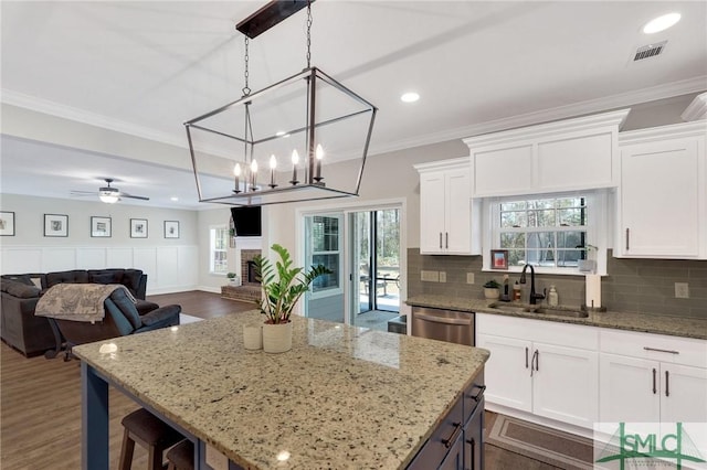 kitchen featuring dishwasher, crown molding, a fireplace, white cabinetry, and a sink