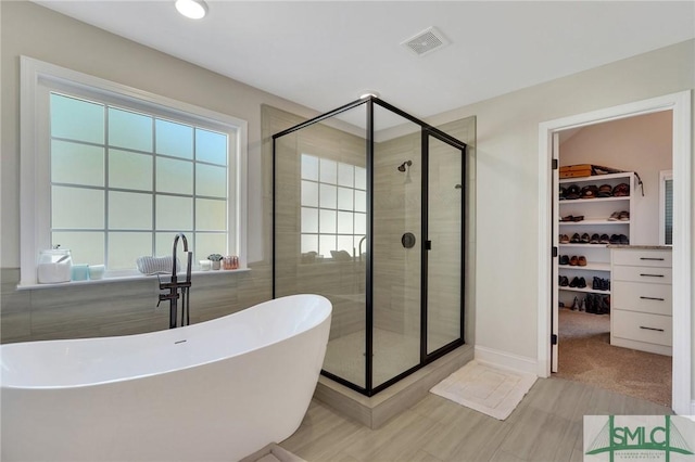 bathroom with a stall shower, a spacious closet, visible vents, and a soaking tub