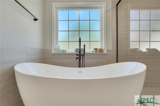 bathroom featuring plenty of natural light, a freestanding bath, and tile walls