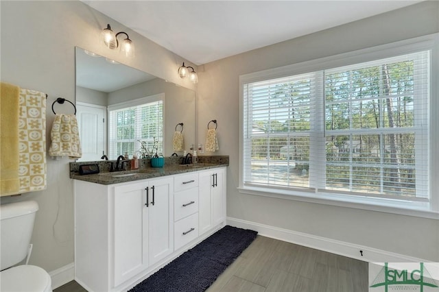 full bath featuring baseboards, a sink, toilet, and double vanity