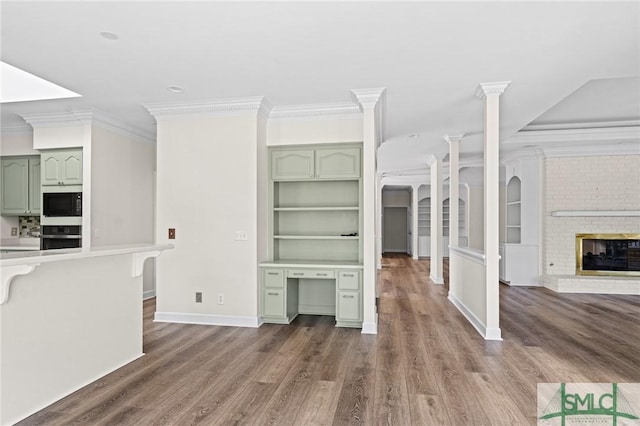 unfurnished living room featuring ornamental molding, a fireplace, decorative columns, and wood finished floors