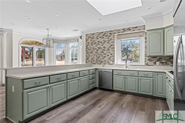 kitchen with a peninsula, crown molding, stainless steel dishwasher, green cabinets, and a wealth of natural light