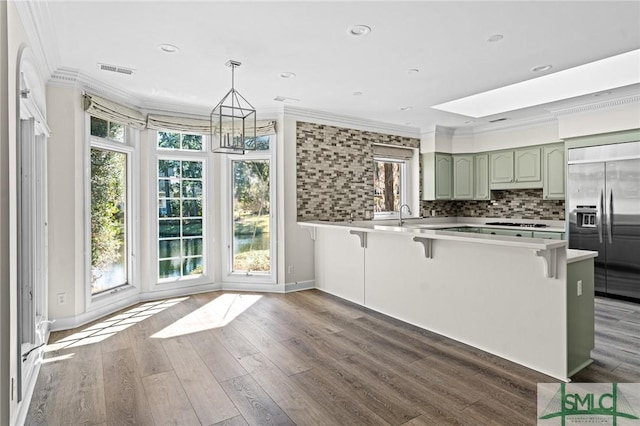 kitchen with ornamental molding, wood finished floors, green cabinetry, built in refrigerator, and a kitchen breakfast bar