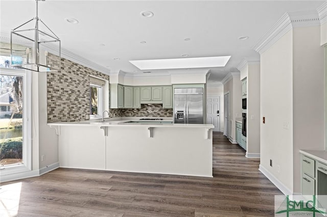 kitchen with a breakfast bar, a peninsula, stainless steel built in fridge, crown molding, and backsplash