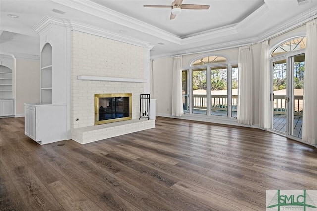 unfurnished living room with dark wood finished floors, a ceiling fan, a brick fireplace, a raised ceiling, and crown molding